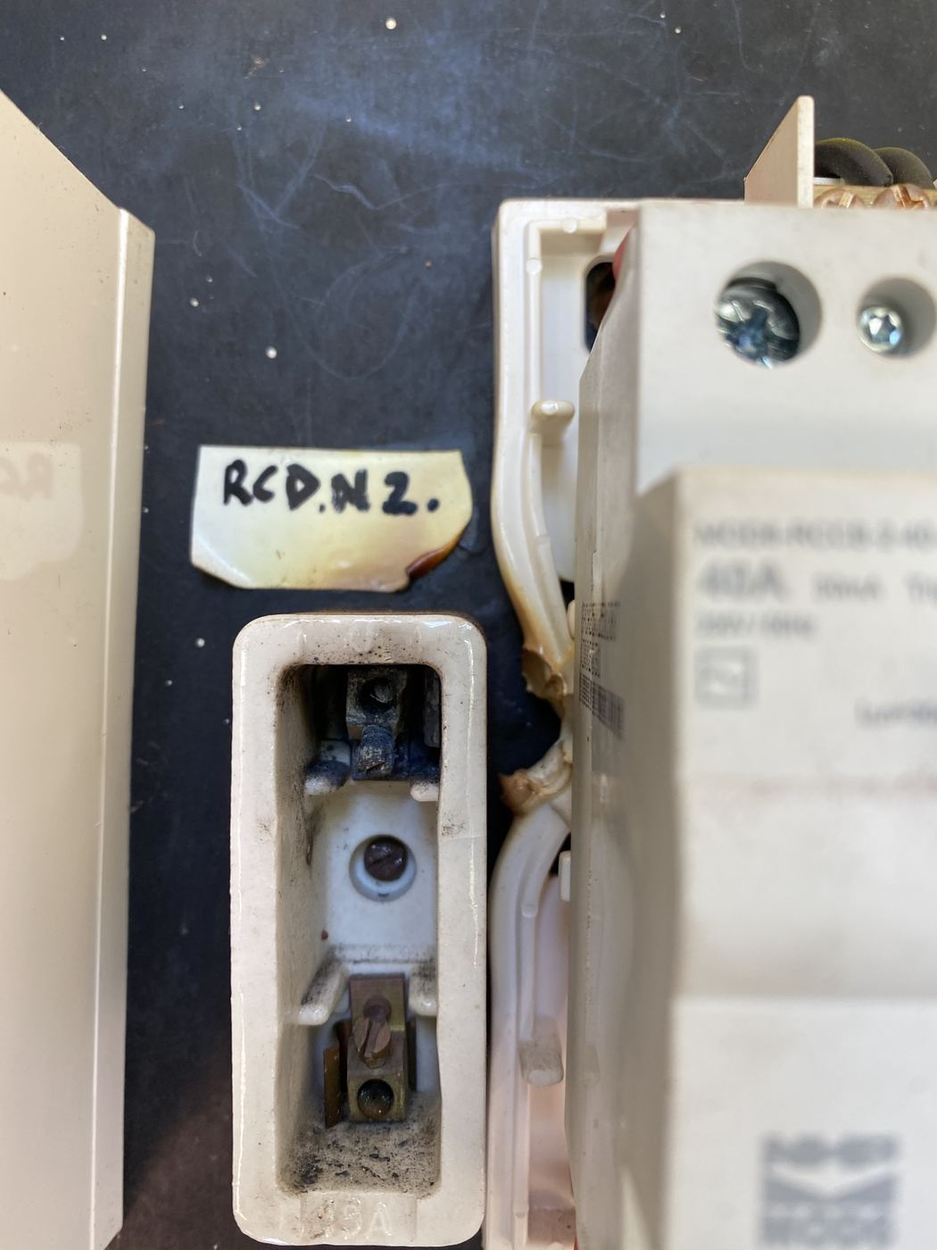 Old ceramic fuse holder with scorched label and melted cable insulation in a switchboard