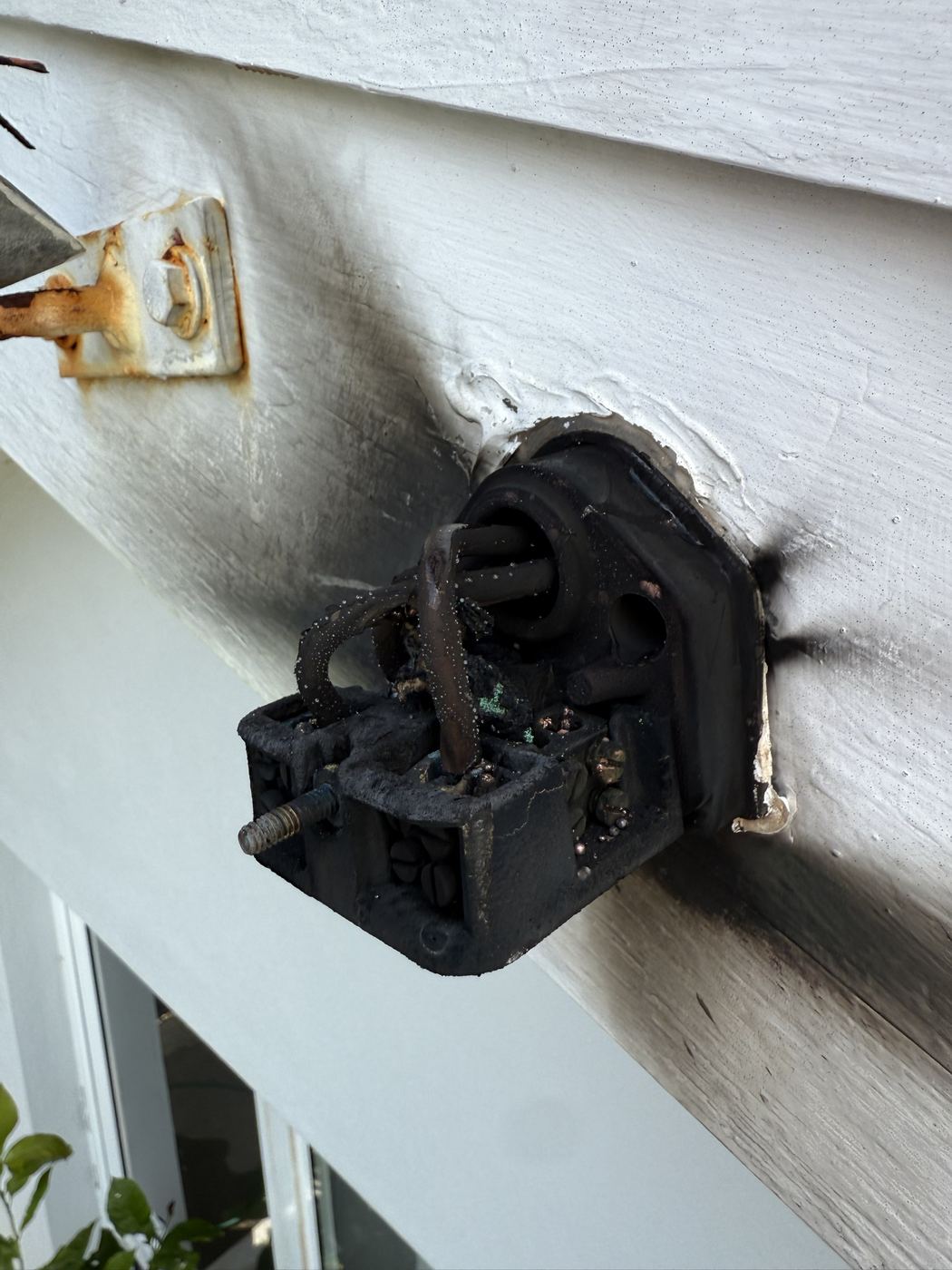 Burnt-out service connection box under timber eaves with scorch marks