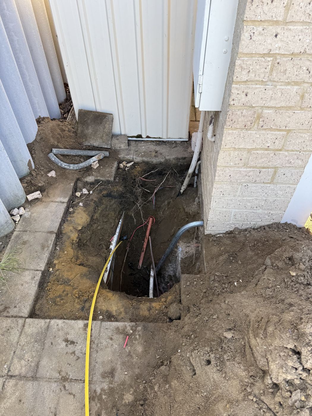 Trench dug beside a meter box to expose underground supply cables