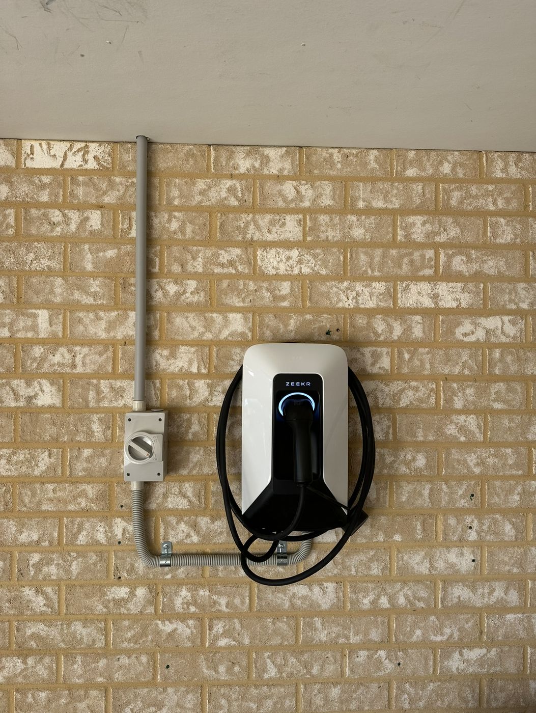 Zeekr EV charger on a brick garage wall with a local isolator and conduit