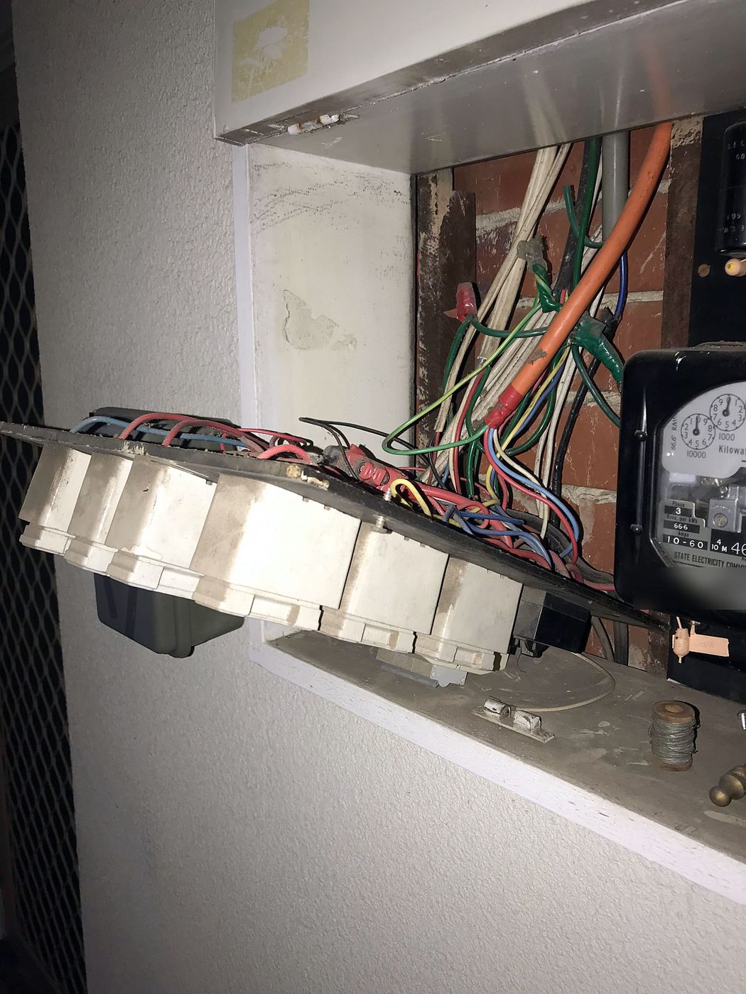 Old switchboard panel pulled forward from the meter box, showing old fuses and wiring