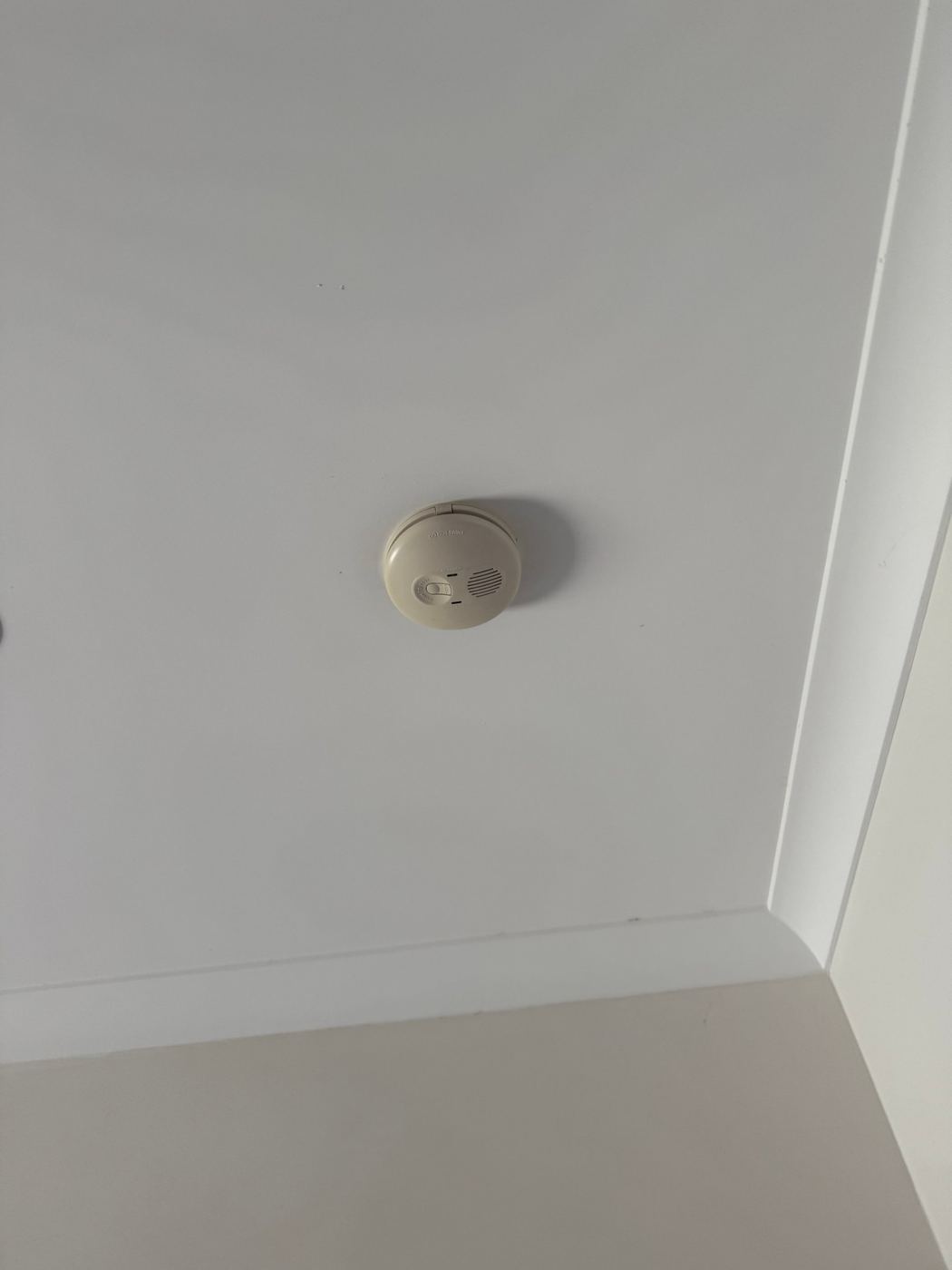 Old discoloured hard-wired smoke alarm on a ceiling
